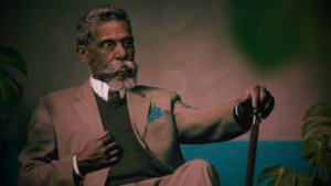 Machado de Assis, escritor brasileiro, sentada em um poltrona, segurando sua bengala